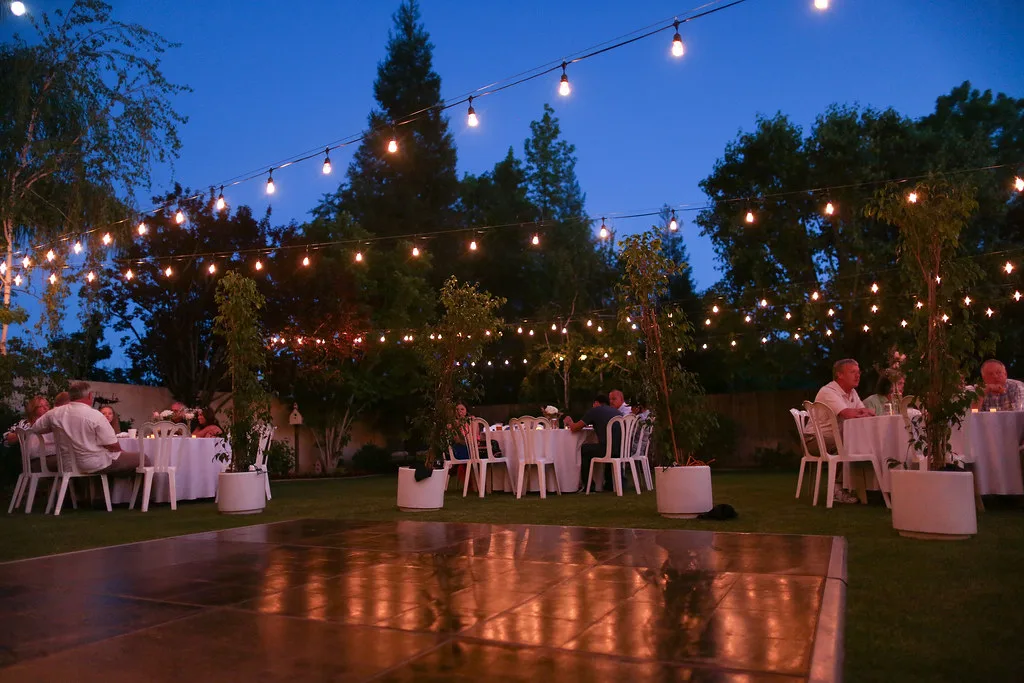 String lights hanging over tables at an outdoor evening wedding reception